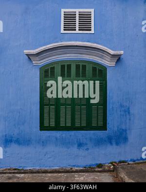 Green wooden window shutters on a vibrant blue wall in the historic district of Hoi An Ancient Town, a UNESCO World Heritage site in Vietnam Stock Photo