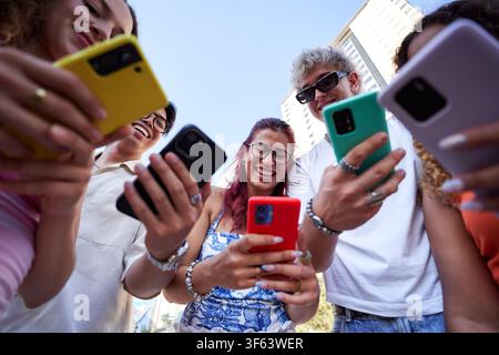People connected to their phones, laughing and chatting together in circle outdoors. Stock Photo