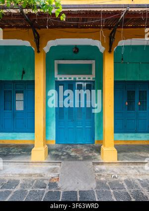 Colorful facade of traditional shophouse architecture with vibrant blue shutters and yellow columns in Hoi An Ancient Town, Vietnam Stock Photo