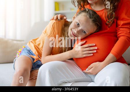 Closeup of smiling girl resting her head on her pregnant mothers belly Stock Photo