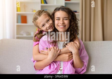 Smiling daughter hugging mother from behind, posing together on sofa at home Stock Photo