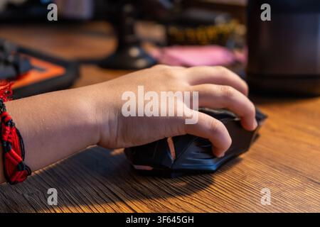 A child's hand playing with a mouse in front of a computer at a wooden desk Stock Photo