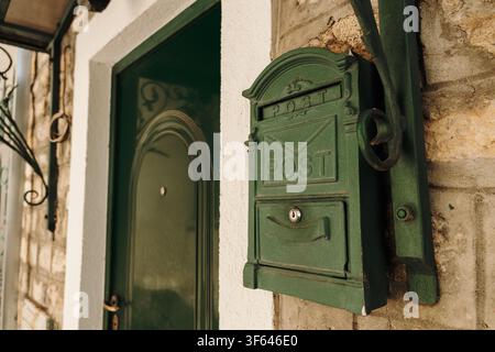 Vintage green mailbox is mounted beside a traditional entrance on a stone house. Decorative details reflect the charm of Mediterranean architecture. Stock Photo