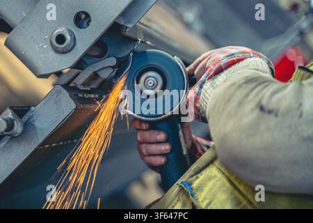 Close-up of worker using angle grinder to polish and smooth metal structure with orange sparks flying in workshop Stock Photo