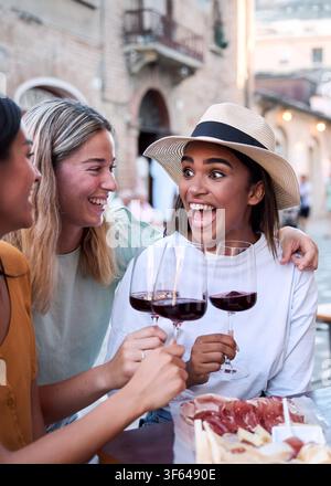 Happy multi-ethnic women friends toasting red wine glasses at outdoor bar in european city Stock Photo