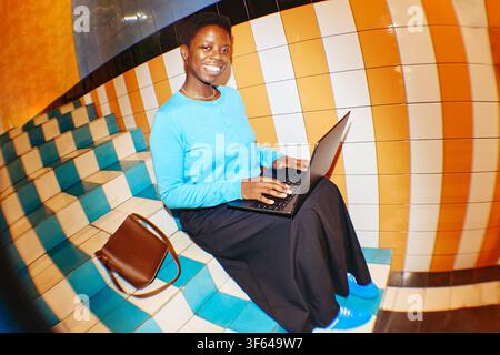 Portrait of Smiling Black Woman Using Laptop on Colorful Stairs Stock Photo