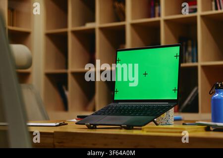 Laptop with Green Screen on Wooden Desk in Modern Office Stock Photo