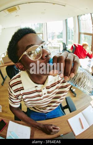 Black Man Drinking Water from Bottle in Office Stock Photo