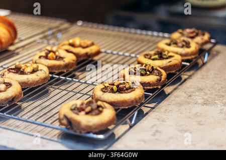 Assorted cookies with creamy centers topped with roasted pistachios and caramelized hazelnuts on a metal rack Stock Photo