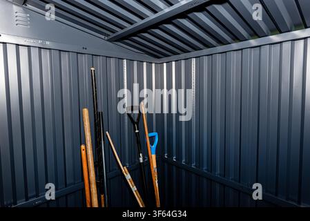 Interior of a corrugated sheet metal shed with various long handled gardening implements Stock Photo