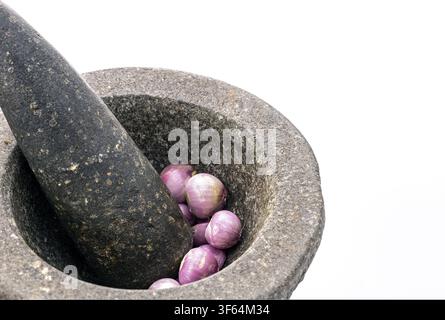 Traditional granite stone mortar and pestle with fresh red shallots inside, ready to grind Asian curry paste, isolated on white background Stock Photo
