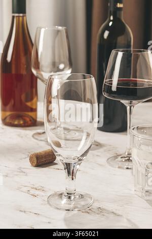 A table displays various wine glasses alongside a bottle of wine. Some glasses are empty while others hold red or white wine. A cork lies nearby on th Stock Photo