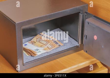 Euro cash money stack lying inside open metal safe box placed on wooden shelf in hotel room cabinet for financial security savings protection concept. Stock Photo