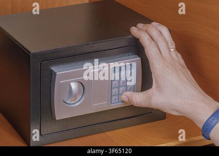 Man hand enters combination PIN code on electronic safe box digital keypad panel inside wooden cabinet shelf for secure personal item access managemen Stock Photo