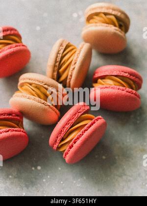 Freshly baked pink and beige French macarons filled with caramel cream on gray background Stock Photo