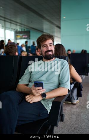 Happy man sitting using phone while waiting for his flight at the airport. Stock Photo