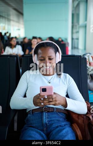 Woman smiling, listening to music, waiting at airport terminal. Stock Photo