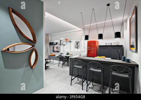 Contemporary kitchen in a Turin apartment converted from office to residential use, with island, pendant lights, red refrigerator and decorative mirro Stock Photo