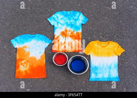 Colorful tie-dye t-shirts and bowls with liquid dye laid out on a white surface, showcasing creative DIY fabric coloring crafts and summer fashion pro Stock Photo