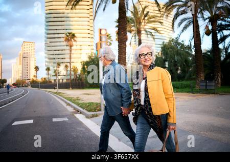 Senior couple holding hands while crossing modern city street Stock Photo
