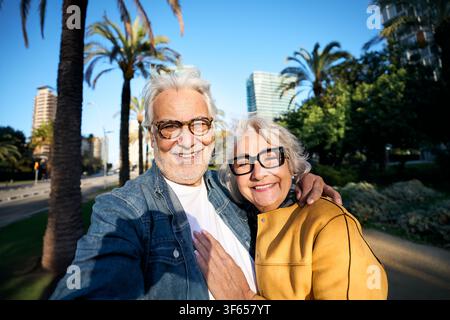 Happy senior couple taking selfie together in sunny city park Stock Photo