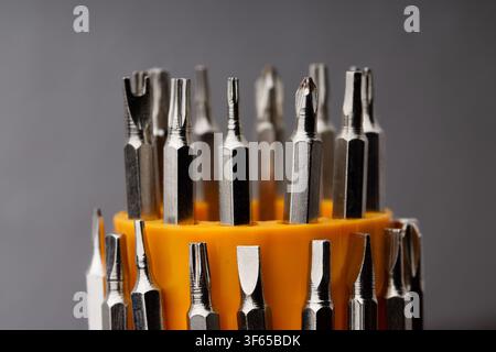 Close-up of a screw bits set with various screwdriver tips in an orange plastic holder under soft studio lighting on a grey background. Stock Photo