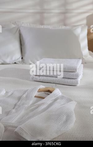 Clean bathrobe and towels on bed indoors Stock Photo