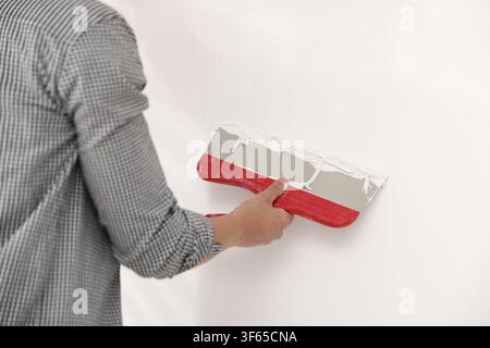 Worker plastering white wall with putty knife indoors, closeup Stock Photo