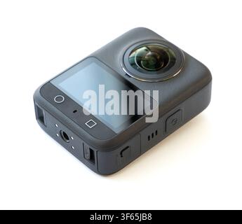 A compact black action camera with a prominent fisheye lens is positioned at an angle on a clean white surface Stock Photo