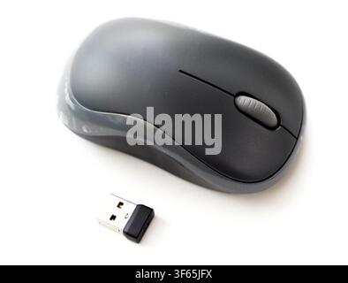 A dark gray wireless computer mouse is shown next to its small USB nano receiver on a plain white background Stock Photo