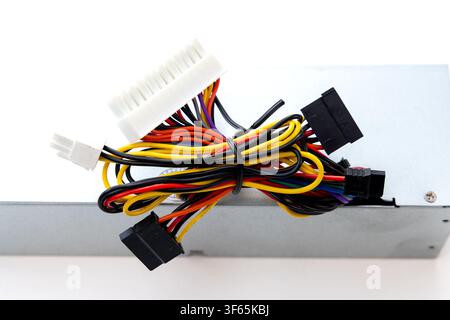 A computer power supply unit sits isolated against a white background with a tangled bundle of colorful cables resting on top Stock Photo