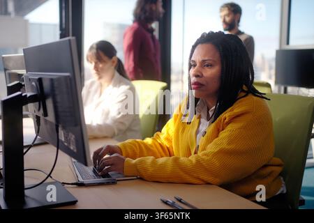 Focused Black businesswoman working on laptop in modern open office Stock Photo