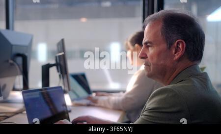 Businessman thinking and working on laptop in office with colleagues Stock Photo