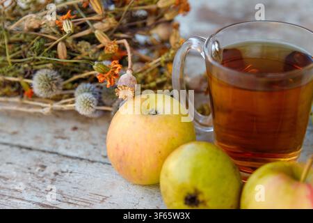 Dry healing herbs bouquet, cup of herbal tea and some fresh fruits, apples and pears on rustic background. Stock Photo