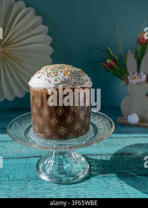 Freshly baked traditional Easter bread displayed on a glass cake stand with spring flowers on a rustic wooden table Stock Photo