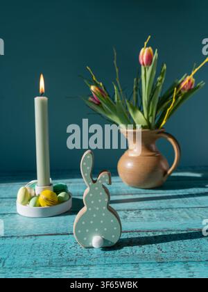 Minimal Easter arrangement with spring tulips ceramic bunny decorated eggs and a lit candle on a rustic wooden table Stock Photo