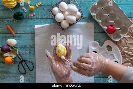 Human hands decorating Easter eggs with colorful dye surrounded by festive Easter decorations on a tabletop Stock Photo