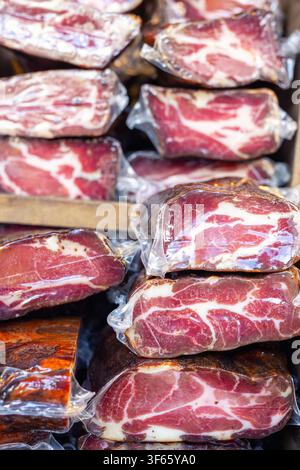 Vacuum-sealed cured meat pieces form layered stacks with rich marbling and deep color. market display shows texture, freshness and artisanal quality Stock Photo