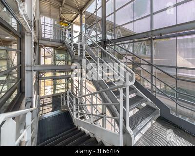 Industrial steel pedestrian overpass and multi-level staircase at Alba railway station, Italy. Modern architectural structure featuring galvanized met Stock Photo