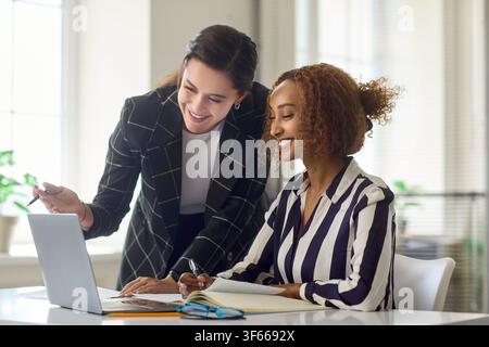 Two businesswomen collaborating at laptop in modern office, teamwork and planning Stock Photo