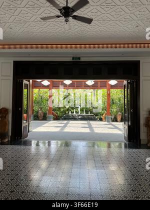 Resort lobby doorway looking out to tropical courtyard. View from an elegant indoor hotel lobby with patterned tile flooring through an open doorway t Stock Photo