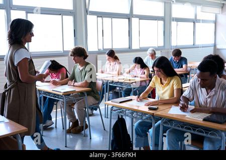 Students taking exam while teacher supervises in classroom Stock Photo