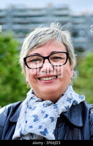 Portrait of joyful senior grey woman glasses posing happy with unfocused background urban garden. Stock Photo