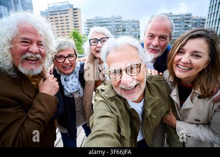 Selfie group mature Caucasian people taking smiling photo together with city in background.  Stock Photo