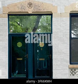 Dark teal double entrance doors with rrund windows beneath transom contrast with a pale brick facade on a Chicago building. Stock Photo
