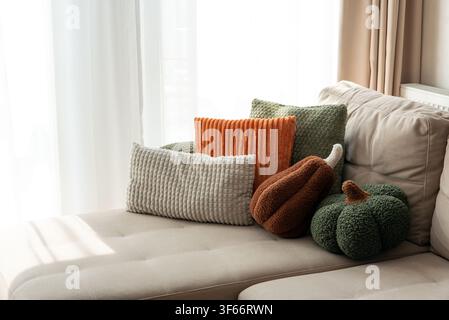 Warm light illuminates a collection of plush textured cushions and decorative pumpkin pillows arranged on a neutral-toned sofa, creating a comfortable Stock Photo