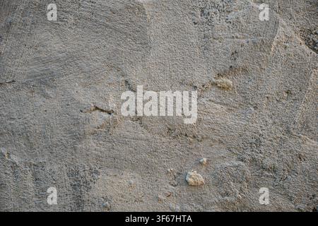 Close-up of an aged gray plaster wall with worn, peeling and uneven texture, cracks and natural imperfections creating an authentic distressed backgro Stock Photo