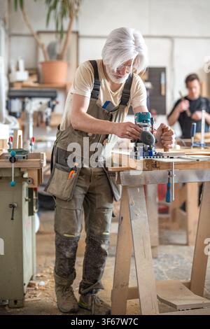 Carpenter works with handheld electric router machine on rail with additional stabilization handle. Stock Photo