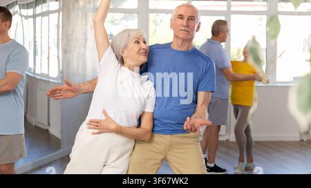 Positive senior woman and man practicing tango dance moves as a couple during a group celebration in dance studio Stock Photo