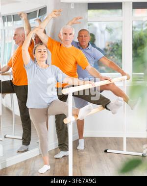 Dedicated mature females and males ballet dancer performing leg stretch at barre with concentration and grace in choreography studio during group Stock Photo